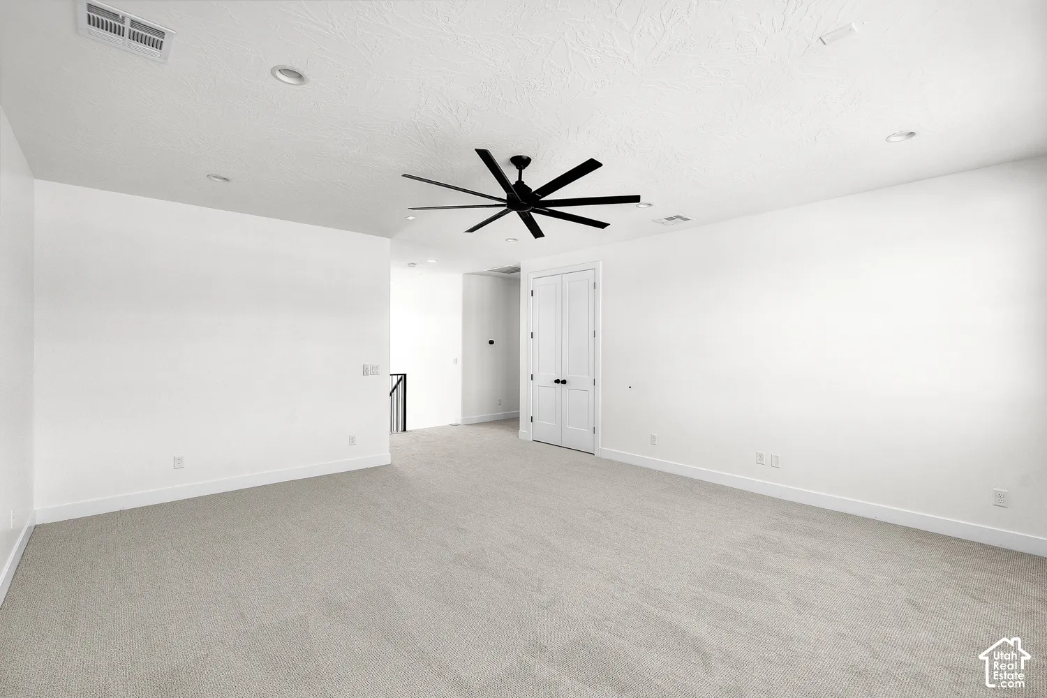 Spacious room featuring light-toned carpeting, a contemporary ceiling fan with black blades, recessed lighting, and a white paneled door with black hardware