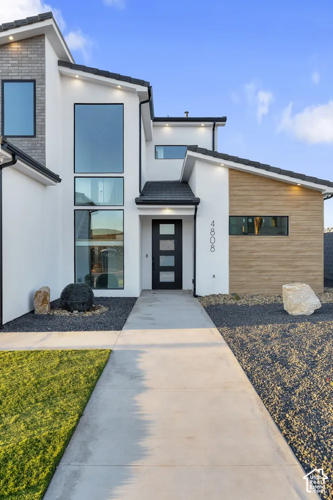 Modern exterior featuring a stucco finish, stone accents, wood-look siding, a flat roofline, and large picture windows