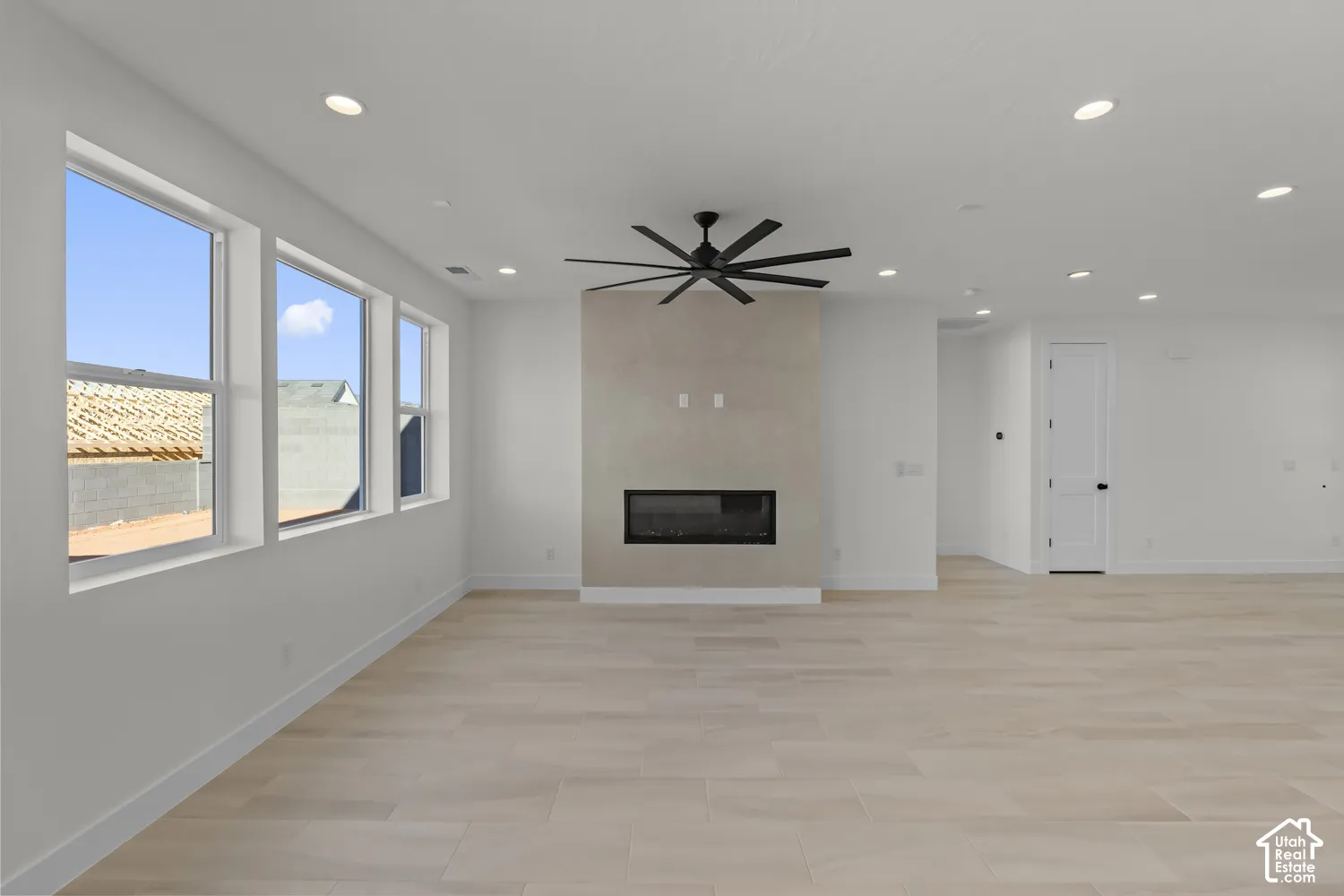 Expansive living space featuring light-toned flooring, recessed lighting, and a modern fireplace with a textured surround