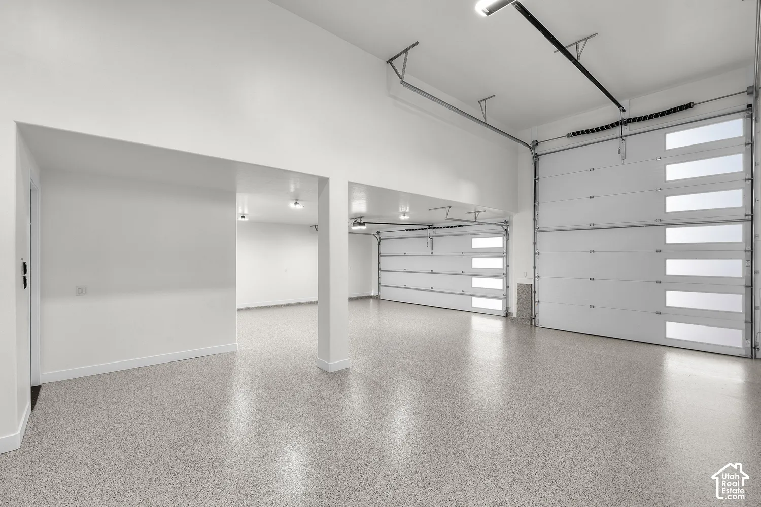 Spacious interior with high ceilings, two modern garage doors featuring frosted glass panels, and durable speckled epoxy flooring