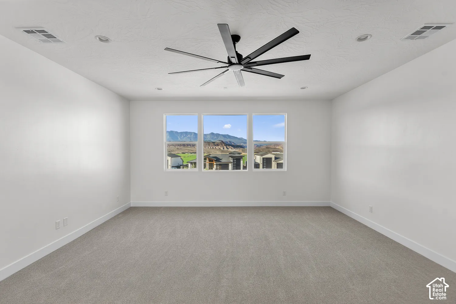 Spacious room featuring gray carpet flooring, white walls, and a modern ceiling fan with five black blades