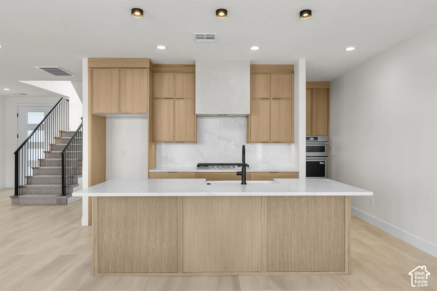 Modern kitchen featuring light wood-finish cabinetry, a large center island with a white countertop, and a built-in oven and microwave