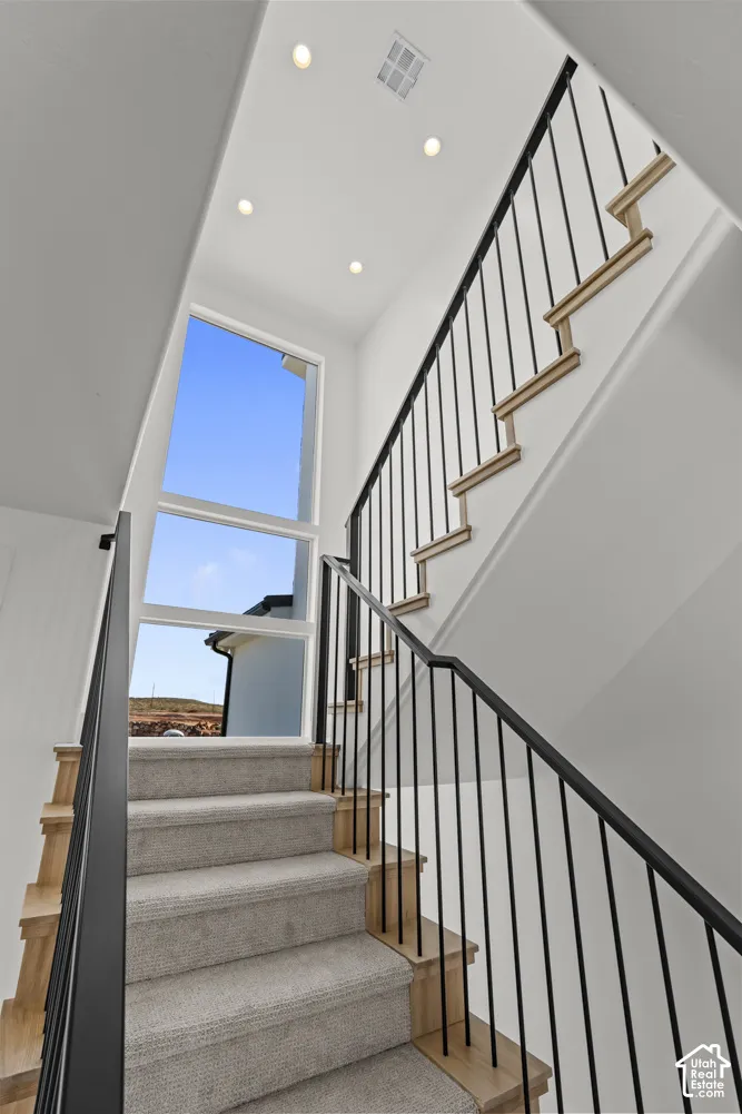 Open staircase featuring a black metal railing, carpeted treads, and wood-finish risers