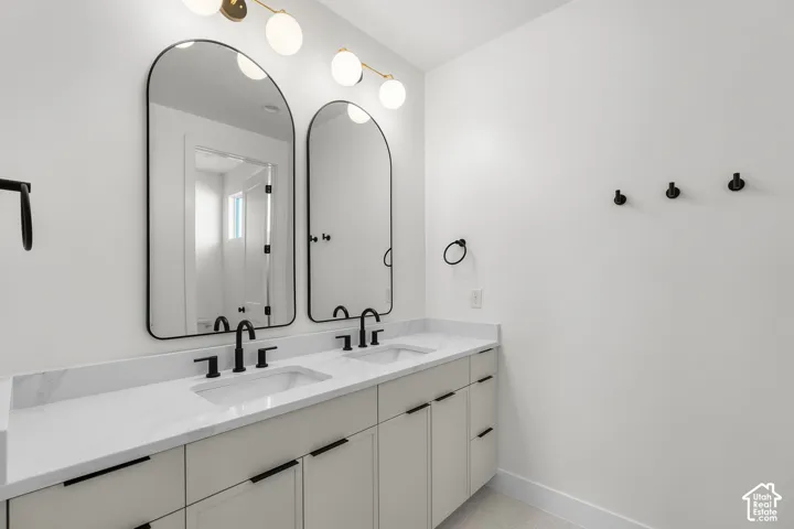 Double vanity with white countertops, matte black fixtures, arched mirrors, and a multi-bulb light fixture