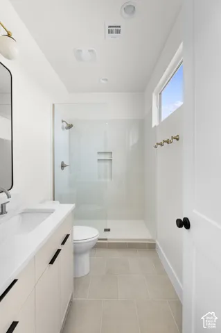 Walk-in shower with glass enclosure, single vanity with integrated sink, light-colored tile flooring, and a window for natural light