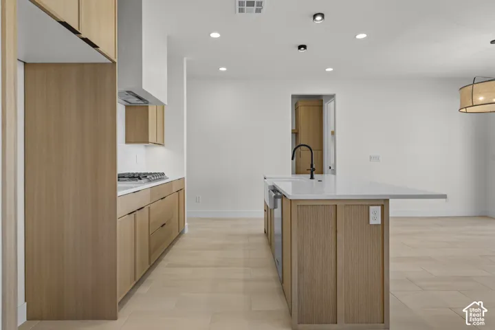 Modern kitchen featuring wood-finish cabinetry, a gas cooktop with a range hood, and light-toned countertops