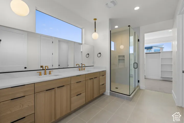 Dual vanity with brass fixtures and wood-finish cabinetry, frameless glass shower enclosure, large transom window, and neutral tile flooring