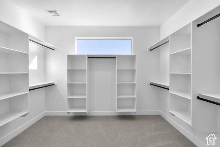 Spacious closet featuring built-in white shelving, hanging rods, and a high window