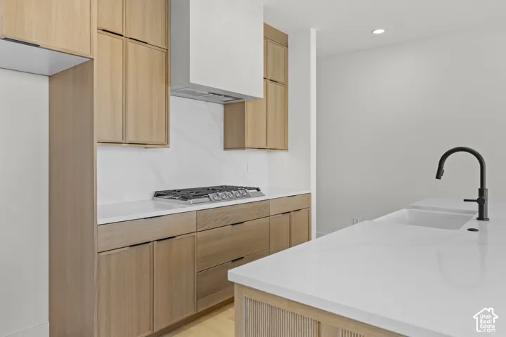 Warm wood-finish cabinetry, white countertops, built-in cooktop, integrated range hood, and a matte black gooseneck faucet