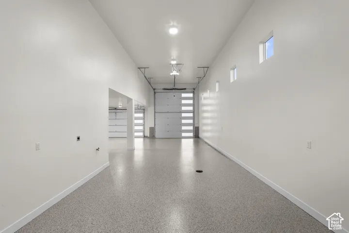 Spacious garage interior featuring polished concrete flooring, abundant natural light from clerestory windows, overhead recessed lighting, and multiple wall-mounted storage shelving units