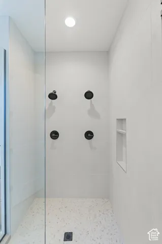 Glass-enclosed shower featuring dual matte black showerheads, integrated niche shelving, white tile walls, and a speckled floor