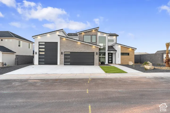 Contemporary exterior featuring a stone and stucco facade, multiple garage doors with frosted glass panels, and a modern front entry with vertical windows