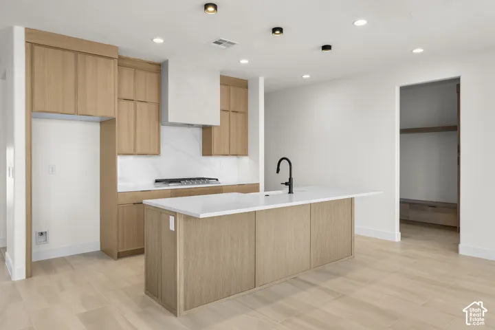 Kitchen featuring wood-finish cabinetry, a large center island with a white countertop and integrated sink, a built-in range, and white tiled backsplash