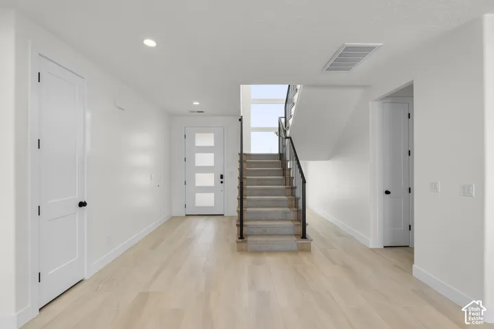 Light wood-finish flooring, recessed ceiling lighting, a contemporary staircase with metal railings, and a front entry door with frosted glass panels