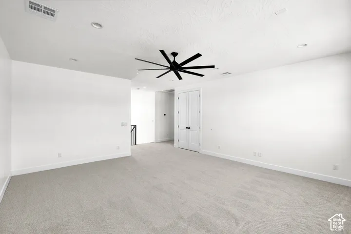 Spacious room featuring light-toned carpeting, a contemporary ceiling fan with black blades, recessed lighting, and a white paneled door with black hardware