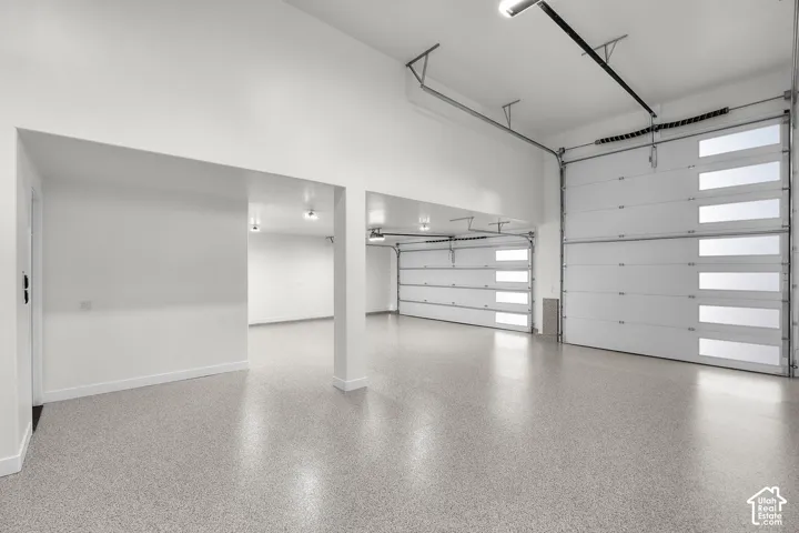 Spacious interior with high ceilings, two modern garage doors featuring frosted glass panels, and durable speckled epoxy flooring
