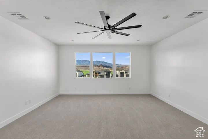 Spacious room featuring gray carpet flooring, white walls, and a modern ceiling fan with five black blades