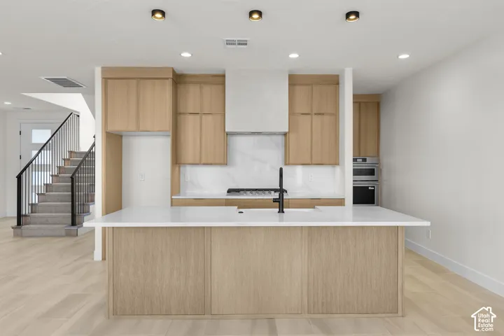 Modern kitchen featuring light wood-finish cabinetry, a large center island with a white countertop, and a built-in oven and microwave