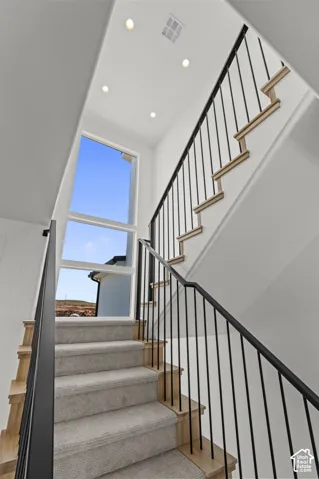 Open staircase featuring a black metal railing, carpeted treads, and wood-finish risers