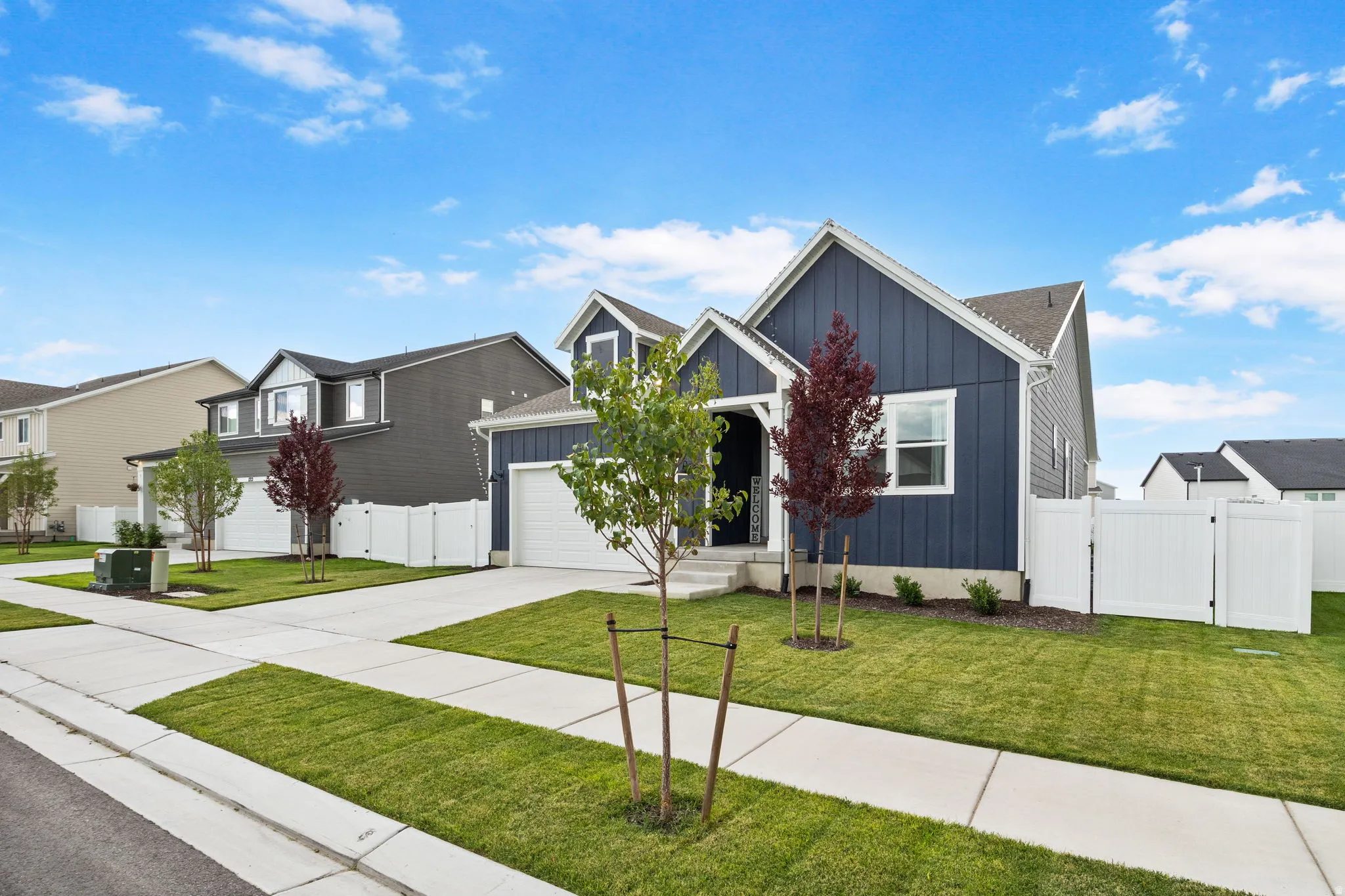 Like new home with attached two-car garage, concrete driveway, manicured lawn, and white privacy fencing