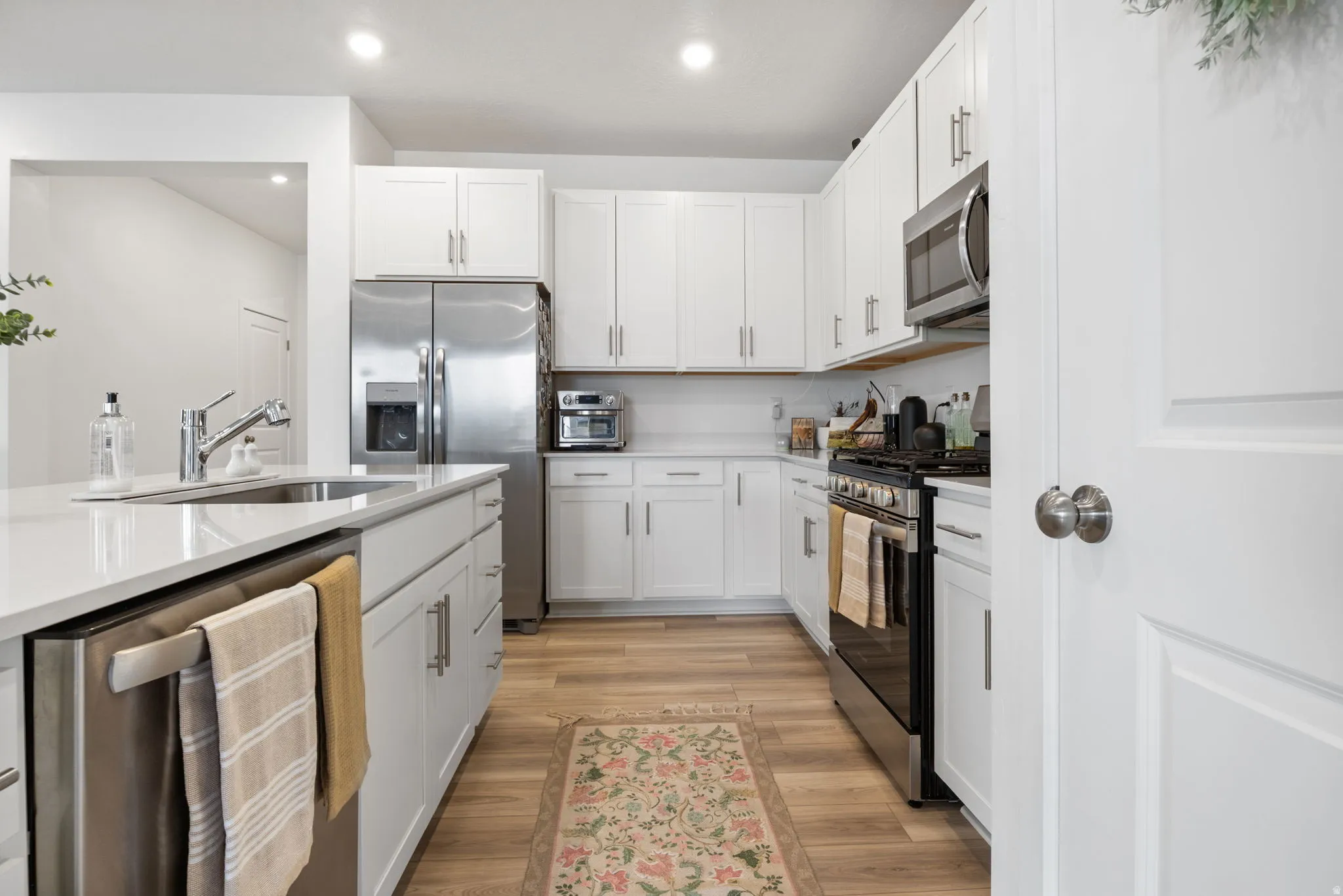 Kitchen featuring white cabinetry, stainless steel appliances, light-toned wood-finish flooring, recessed lighting, and a white countertop island with a stainless-steel sink