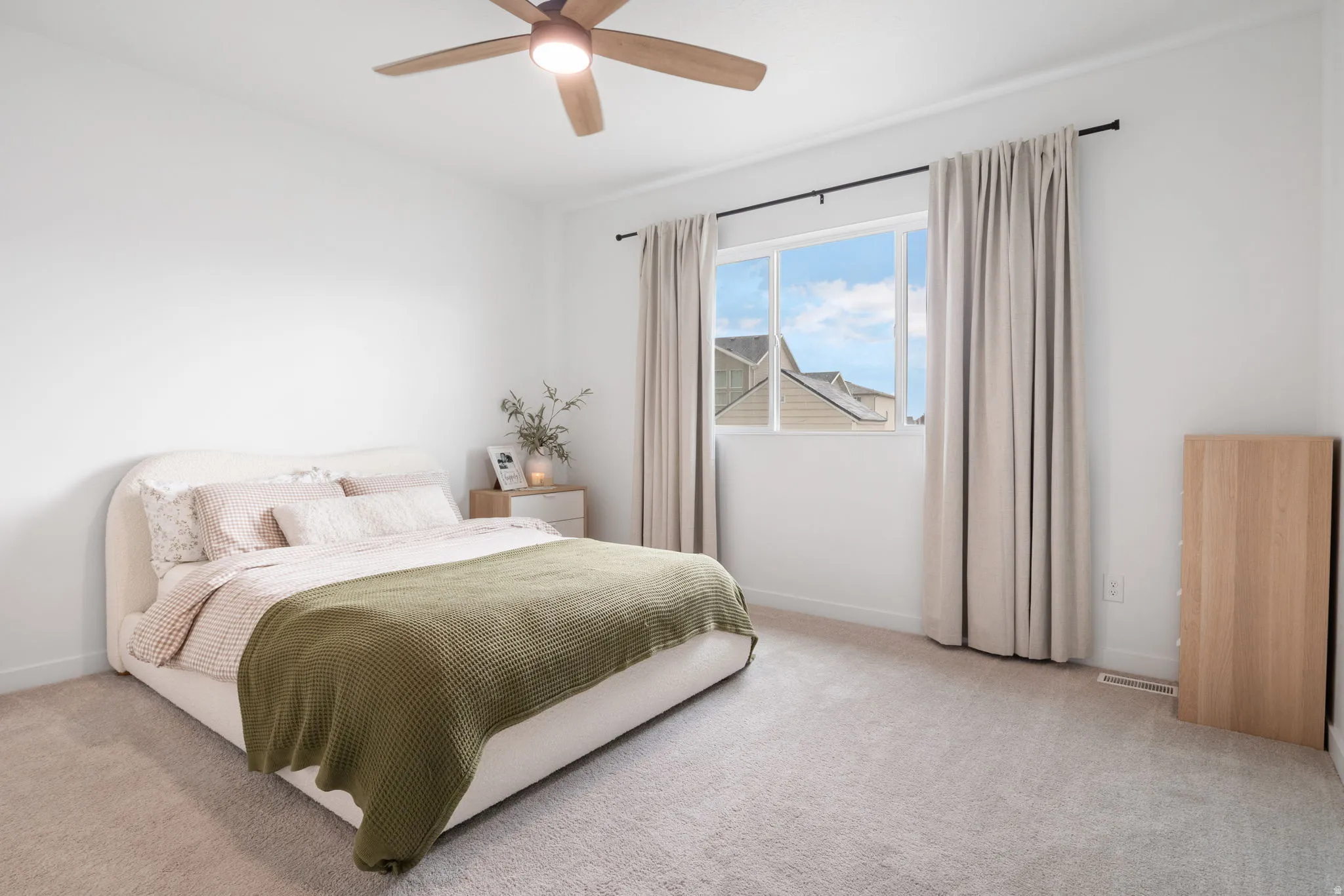 Large Primary bedroom with plush carpeted flooring, large window with elegant drapery, and a ceiling fan.