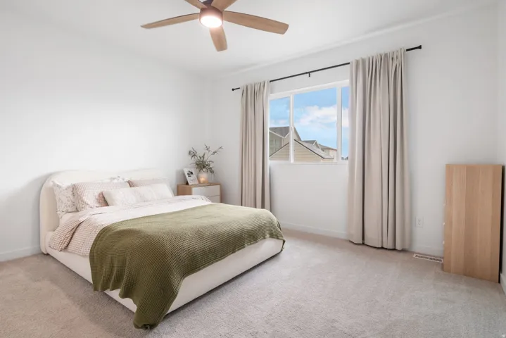 Large Primary bedroom with plush carpeted flooring, large window with elegant drapery, and a ceiling fan.