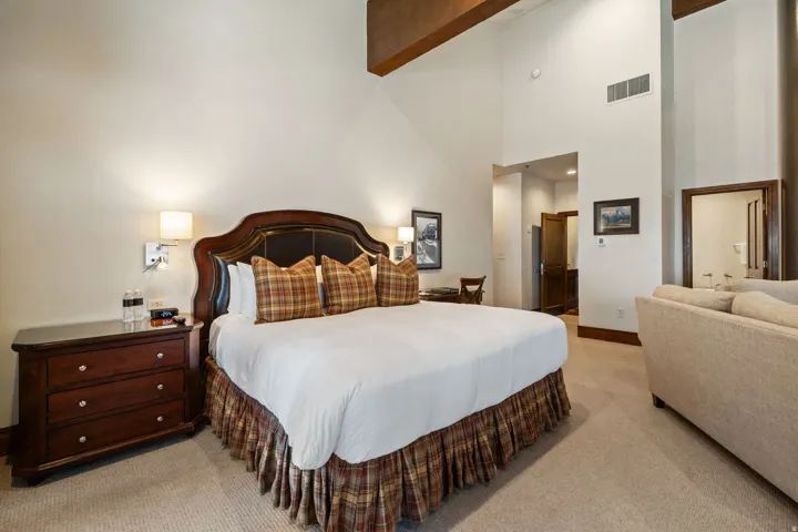 Spacious room featuring vaulted ceilings, exposed wood beams, and a large bed with a dark wood headboard