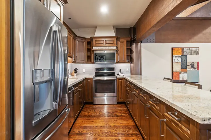Well-appointed kitchen featuring wood-finish cabinetry, stainless steel appliances, granite countertops, and a wood-finish flooring