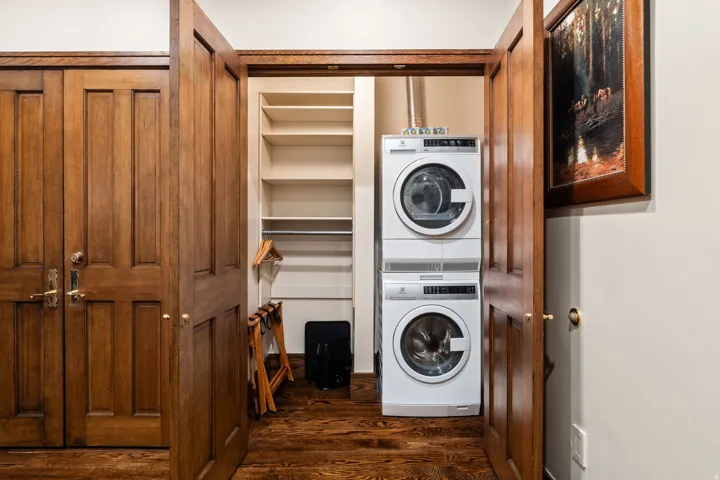 Integrated laundry appliances with wood-finish flooring, built-in shelving, and paneled wood doors