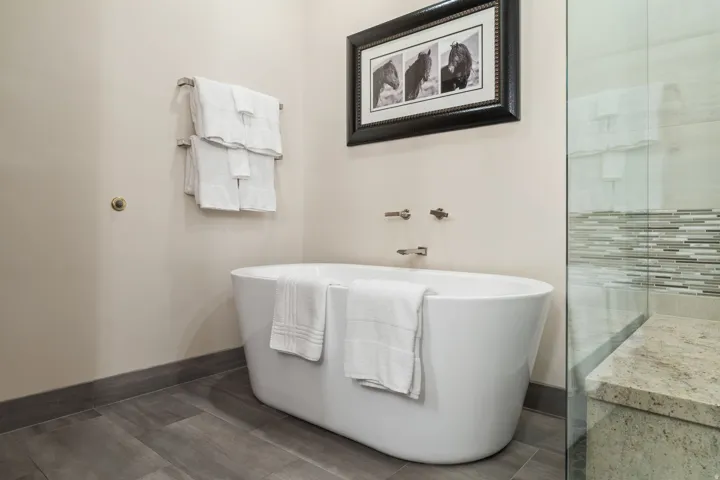 Freestanding soaking tub with wall-mounted fixtures, wood-finish flooring, and a glass-enclosed shower with mosaic tile detailing