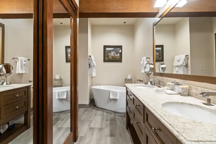 Freestanding soaking tub, wood-finish flooring, dual vanity with undermount sinks, and stone countertops