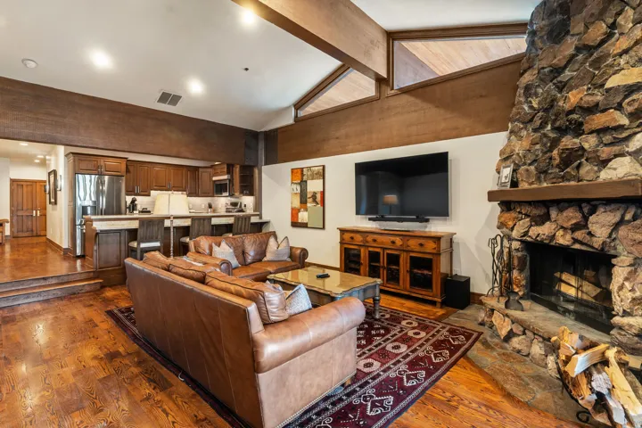 Great room featuring a stone-clad fireplace, wood-finish flooring, and vaulted wood-beamed ceilings