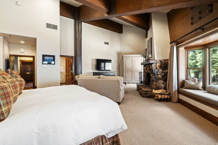 Exposed wood beams, vaulted ceilings, stone fireplace, wood-framed bay window with integrated seating, and neutral carpet flooring