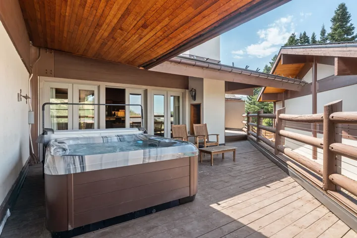 Expansive wood deck with a built-in hot tub, natural wood railing, and direct access through multiple glass panel doors