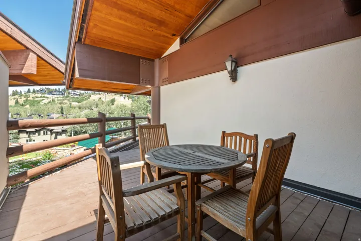 Covered balcony featuring wood-finish decking, wooden railing, and a wall-mounted outdoor light fixture