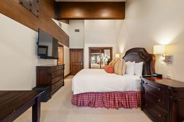 Vaulted ceilings with exposed wood beams, wall-mounted sconces, and built-in closet with mirrored doors
