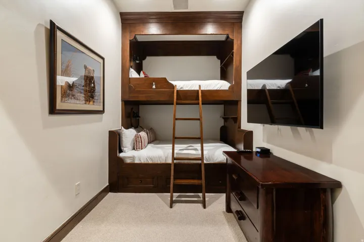 Built-in bunk beds with integrated storage, warm wood-finish cabinetry, wall-mounted television, and light-toned carpeting