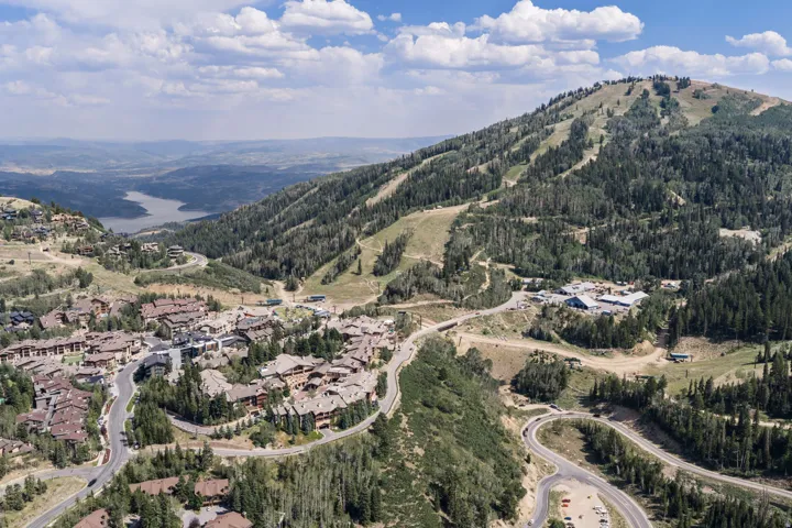 Mountainous terrain with lush tree coverage, a developed community, winding roads, and a visible body of water in the distance