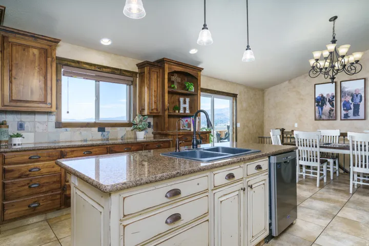 Spacious kitchen featuring wood cabinetry, granite countertops, a center island with sink, stainless steel dishwasher, and tile flooring