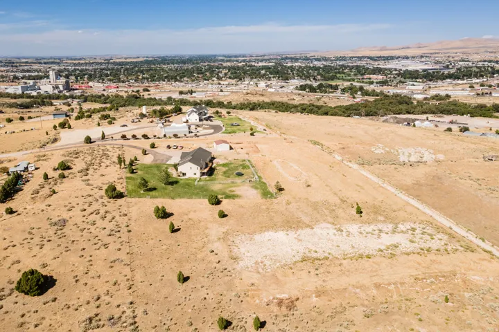 Expansive lot featuring a residential structure, scattered vegetation, and a paved driveway