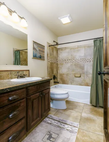 Bathroom featuring a wood vanity with a single basin sink, tiled flooring, tiled shower surround with accent band, and a shower/tub combination