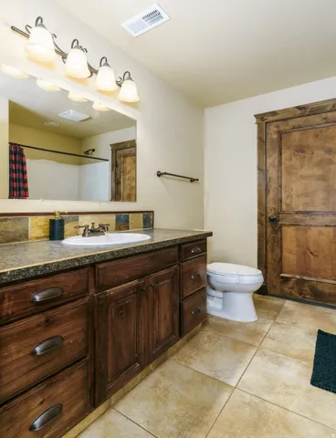 Wood-finish vanity with an integrated sink, dark countertop, and decorative tile backsplash