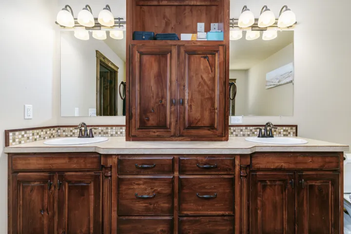 Dual vanity with integral sinks, neutral-toned countertops, rich wood-finish cabinetry, and a mosaic tile backsplash