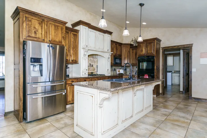 Gourmet kitchen with granite countertops, stainless steel appliances, custom cabinetry, a central island with sink, and tile flooring