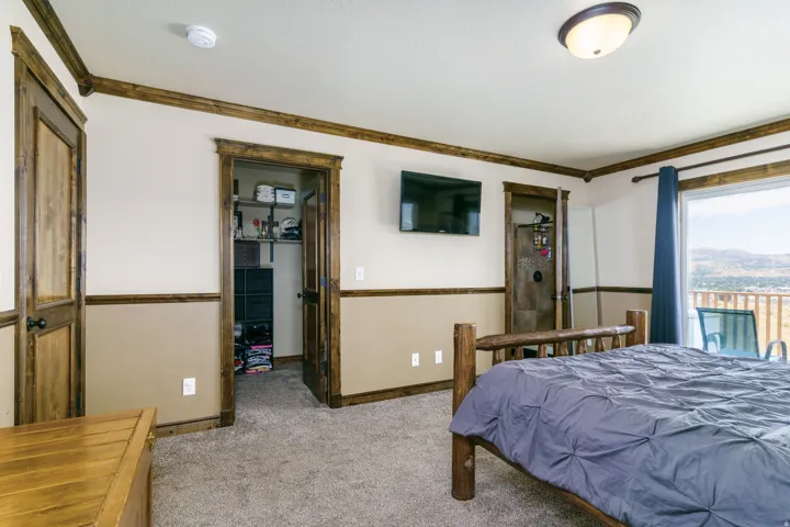 Spacious primary bedroom suite featuring wood-finish flooring, two walk-in closets with wood-frame doors, wall-mounted flat-screen television, recessed ceiling lighting, and expansive windows with panoramic mountain and valley vistas