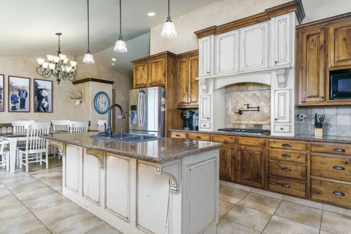 Kitchen with two-tone cabinetry, a central island with a built-in sink, and a range hood feature