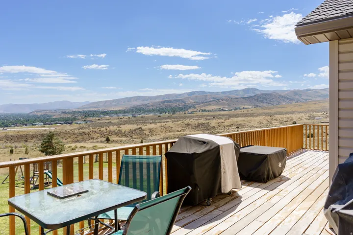 Expansive outdoor deck with wood-finish flooring, natural wood railings, and a wide-ranging mountain backdrop