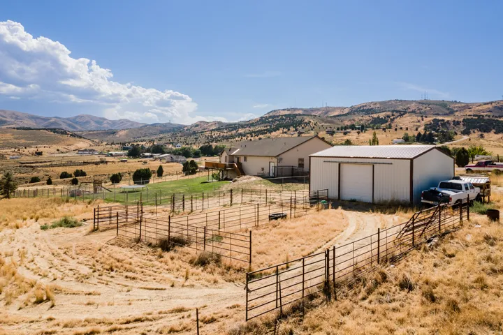 Expansive rural property featuring a main residence with an elevated deck, a large detached metal outbuilding with a roll-up door, and extensive perimeter fencing
