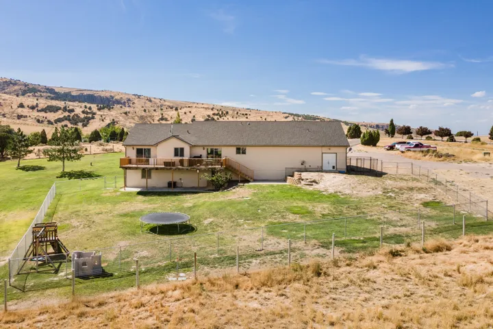 Expansive property featuring a multi-level deck, lower patio, fenced yard, and a distant mountain backdrop